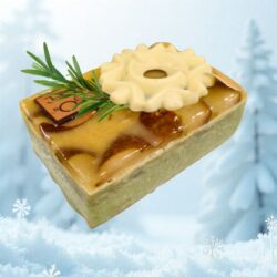 bûche Temps Suspendu de la Maison Gélis, rectangulaire, glaçage doré, flocon de chocolat blanc, brin de romarin et base verte au praliné sur biscuit noisette.